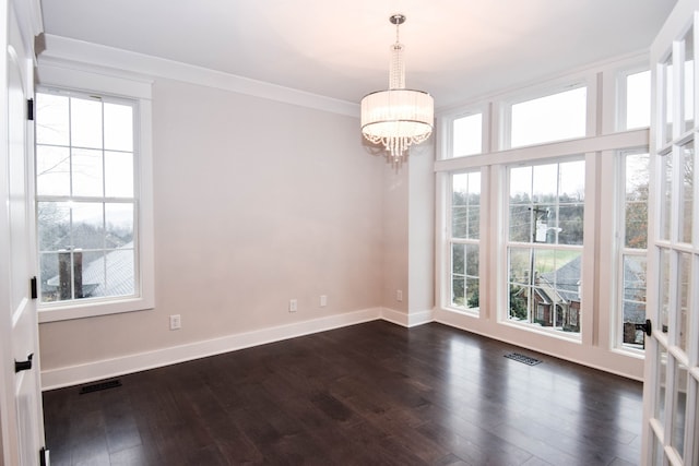 empty room with a chandelier, dark wood finished floors, visible vents, and crown molding