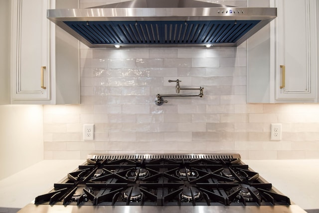 interior space with tasteful backsplash, light countertops, white cabinets, wall chimney range hood, and gas cooktop