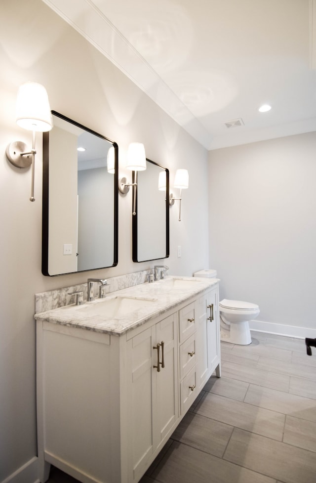 bathroom with visible vents, double vanity, a sink, and toilet