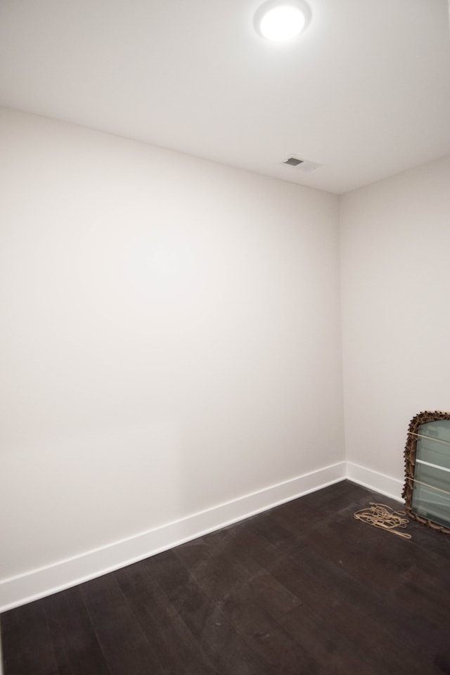 empty room featuring visible vents, baseboards, and dark wood-style flooring