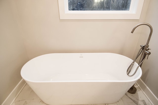 full bath featuring marble finish floor, baseboards, and a freestanding tub