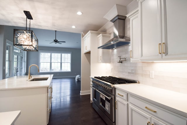 kitchen featuring range with two ovens, tasteful backsplash, white cabinetry, a sink, and wall chimney exhaust hood