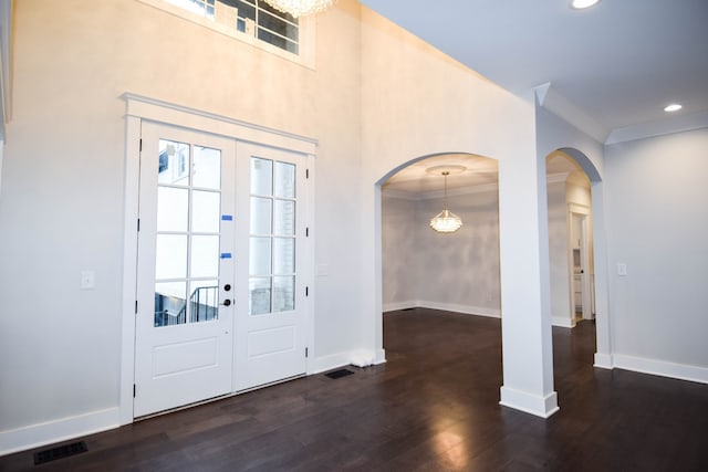 foyer with arched walkways, wood finished floors, visible vents, baseboards, and ornamental molding