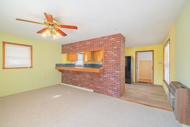 unfurnished living room featuring a healthy amount of sunlight, light wood-type flooring, ceiling fan, and heating unit