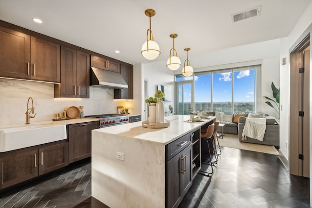 kitchen featuring tasteful backsplash, a kitchen island, dark brown cabinetry, pendant lighting, and sink