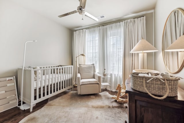 bedroom featuring dark wood-type flooring, a nursery area, and ceiling fan