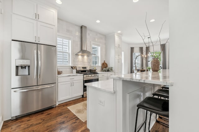 kitchen featuring stainless steel appliances, a kitchen breakfast bar, light stone countertops, white cabinets, and wall chimney range hood