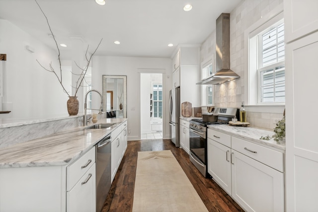 kitchen with white cabinetry, appliances with stainless steel finishes, sink, and wall chimney range hood