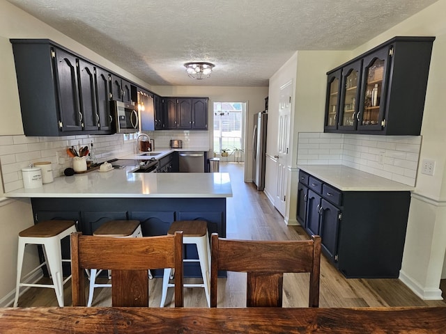 kitchen featuring sink, kitchen peninsula, appliances with stainless steel finishes, tasteful backsplash, and wood-type flooring