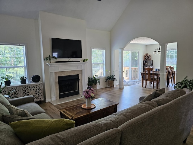 living room featuring ornate columns, light wood-type flooring, plenty of natural light, and a tiled fireplace