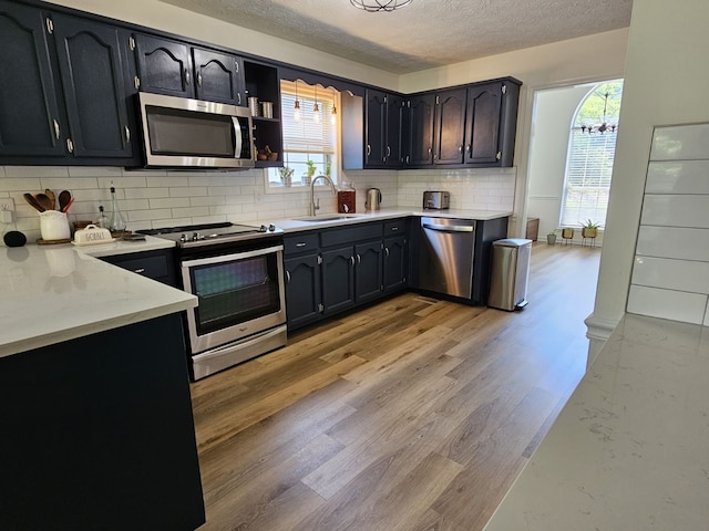 kitchen with stainless steel appliances, sink, a textured ceiling, backsplash, and light wood-type flooring