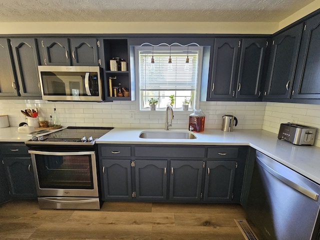 kitchen with light wood-type flooring, appliances with stainless steel finishes, sink, and backsplash