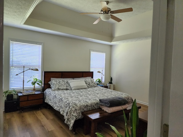 bedroom with a textured ceiling, hardwood / wood-style floors, ceiling fan, and a tray ceiling