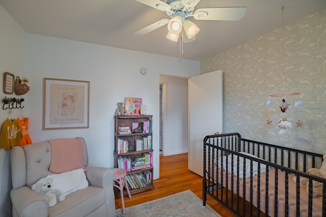 bedroom with light hardwood / wood-style floors, a nursery area, and ceiling fan