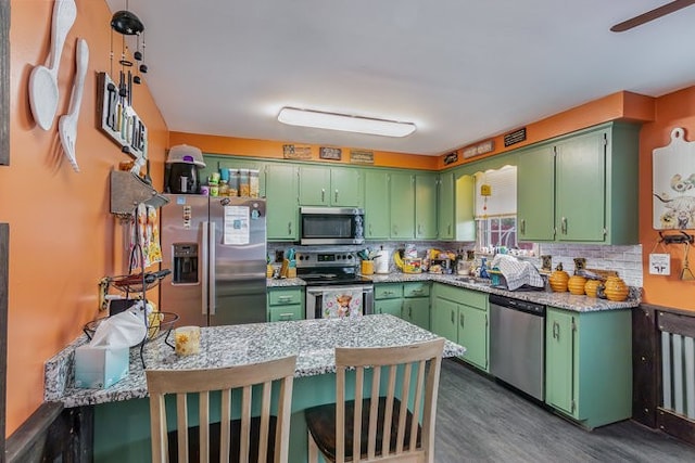 kitchen with stainless steel appliances, a kitchen bar, green cabinetry, and kitchen peninsula