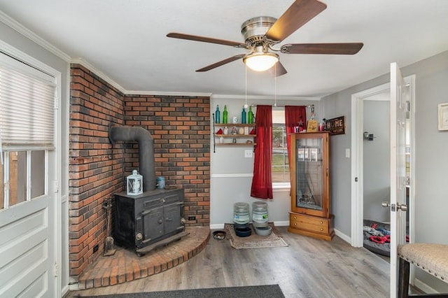 living room featuring ceiling fan, a wood stove, crown molding, and wood-type flooring