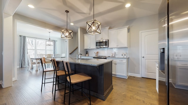 kitchen featuring stainless steel appliances, white cabinets, an island with sink, and pendant lighting