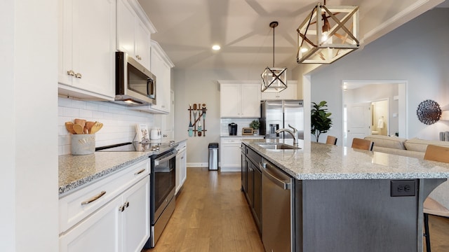 kitchen featuring stainless steel appliances, a center island with sink, white cabinets, hanging light fixtures, and a kitchen breakfast bar