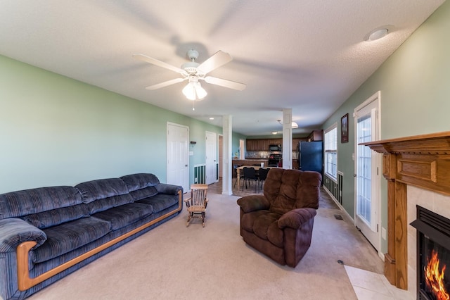 carpeted living room featuring ceiling fan, a tiled fireplace, and a textured ceiling