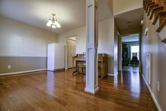 interior space featuring ornate columns, dark hardwood / wood-style flooring, a textured ceiling, and an inviting chandelier