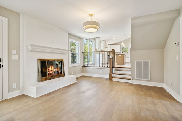 unfurnished living room with a fireplace, light hardwood / wood-style flooring, and lofted ceiling