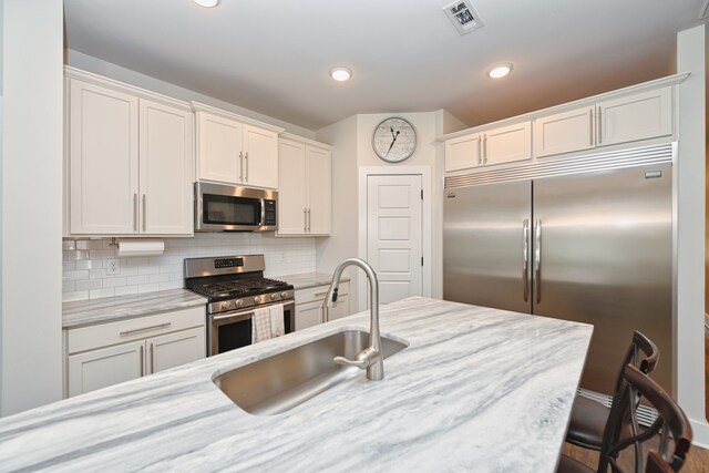 kitchen featuring white cabinets, decorative backsplash, sink, light stone countertops, and appliances with stainless steel finishes