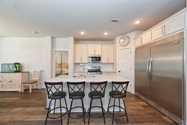 kitchen with stainless steel appliances, sink, white cabinets, a kitchen island with sink, and dark wood-type flooring