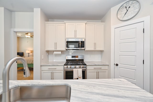 kitchen with stainless steel appliances, sink, light stone counters, white cabinets, and decorative backsplash