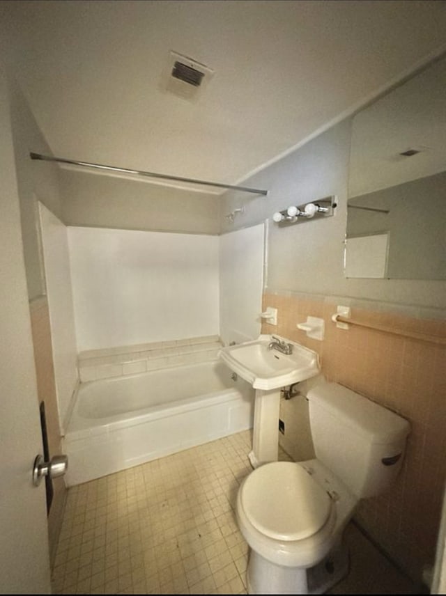 bathroom featuring toilet, shower / tub combination, and tile walls