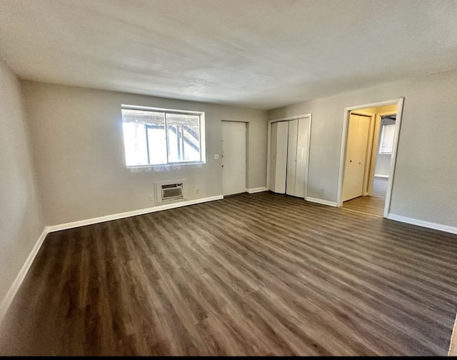 unfurnished bedroom featuring dark hardwood / wood-style flooring, a textured ceiling, a wall unit AC, and two closets