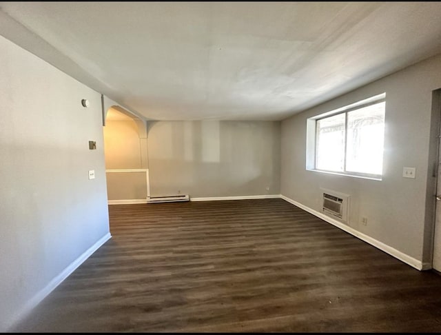 spare room featuring dark hardwood / wood-style flooring, baseboard heating, and a wall unit AC