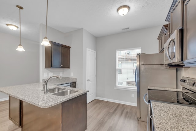 kitchen featuring pendant lighting, sink, light wood-type flooring, a textured ceiling, and stainless steel appliances