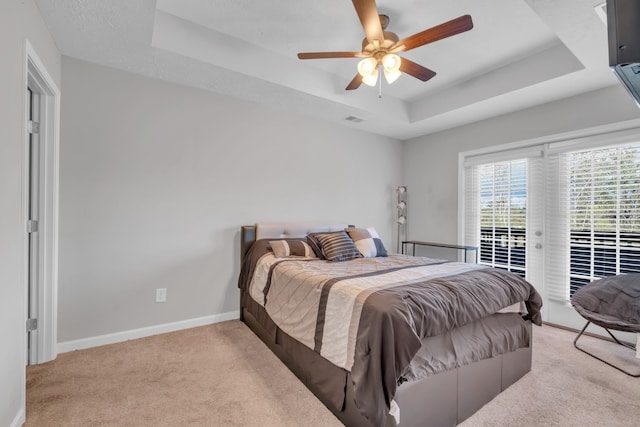 bedroom with a raised ceiling, ceiling fan, and light carpet