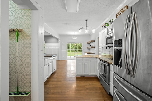 kitchen with appliances with stainless steel finishes, pendant lighting, white cabinets, dark wood-type flooring, and kitchen peninsula