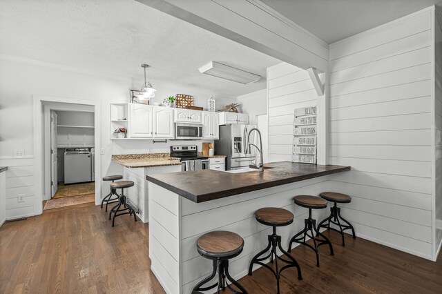 kitchen featuring stainless steel appliances, white cabinetry, kitchen peninsula, a kitchen bar, and decorative light fixtures