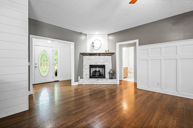 unfurnished living room with a textured ceiling, dark hardwood / wood-style floors, ceiling fan, and a stone fireplace