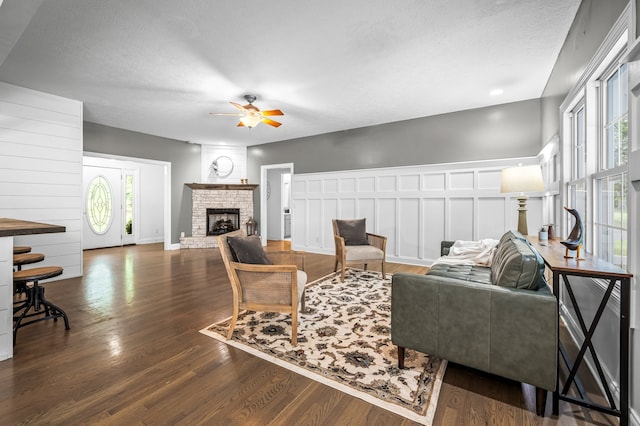 living room featuring a fireplace, dark hardwood / wood-style floors, a textured ceiling, and ceiling fan