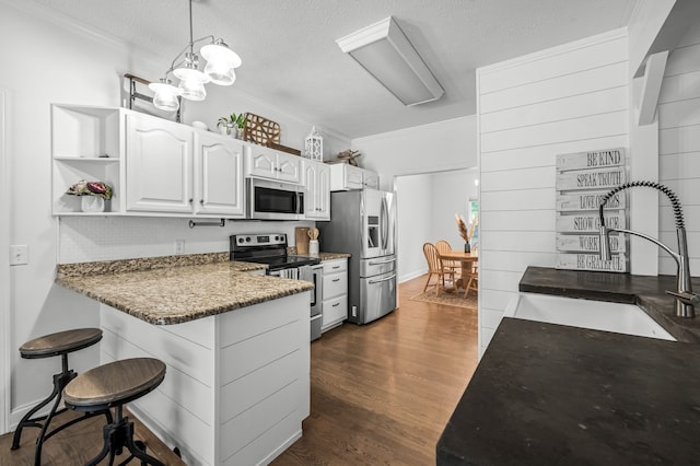 kitchen with appliances with stainless steel finishes, decorative light fixtures, dark hardwood / wood-style flooring, sink, and white cabinets