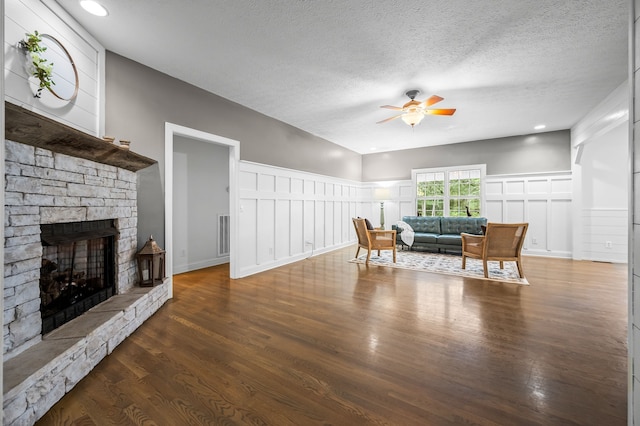 living room featuring ceiling fan, a textured ceiling, dark hardwood / wood-style floors, and a fireplace