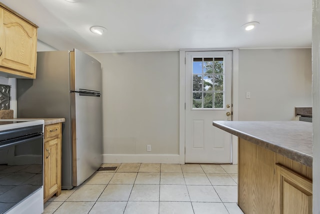 kitchen with light brown cabinets, stove, stainless steel refrigerator, and light tile patterned flooring