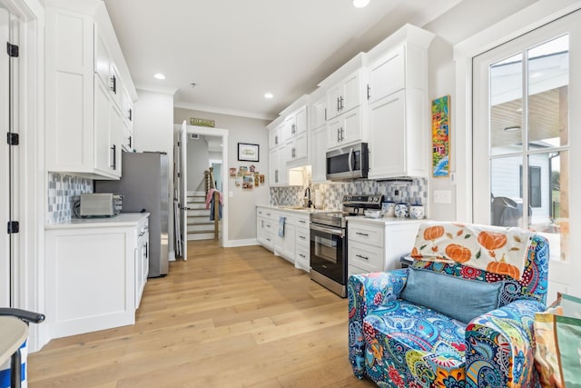 kitchen featuring stainless steel appliances, tasteful backsplash, crown molding, white cabinetry, and light hardwood / wood-style flooring