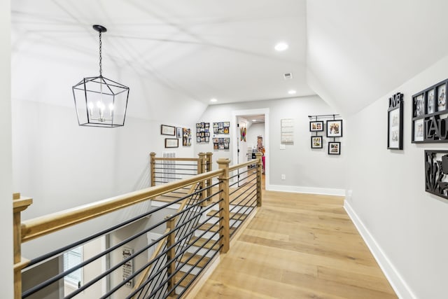 hall featuring lofted ceiling, hardwood / wood-style flooring, and a notable chandelier