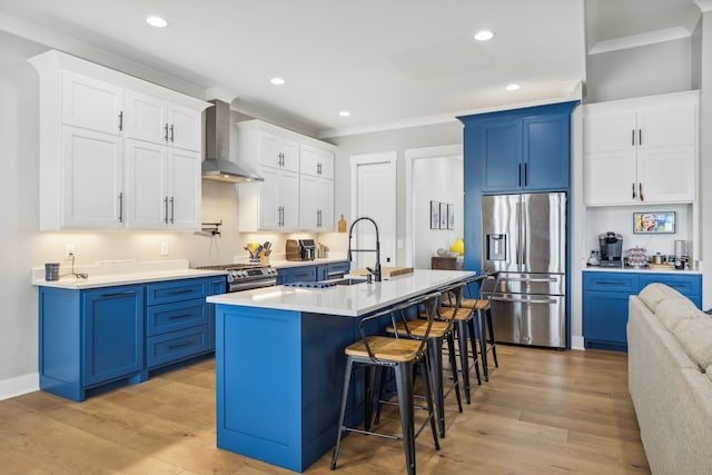 kitchen featuring stainless steel appliances, wall chimney exhaust hood, an island with sink, and light wood-type flooring