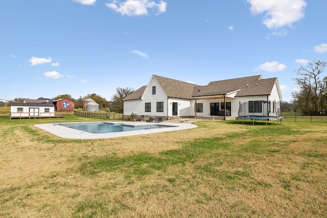 rear view of property with a patio, a fenced in pool, a yard, and a trampoline