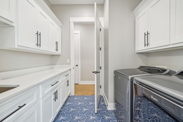 clothes washing area featuring cabinets, washing machine and dryer, and dark tile patterned floors