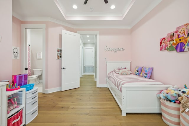 bedroom with ensuite bath, ceiling fan, a raised ceiling, crown molding, and light wood-type flooring