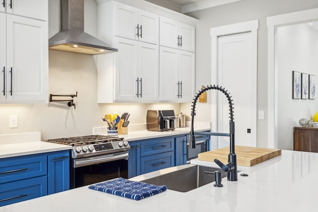 kitchen featuring wall chimney range hood, blue cabinetry, stainless steel gas stove, and white cabinets