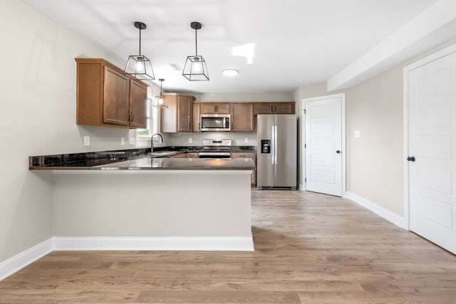 kitchen with stainless steel appliances, decorative light fixtures, kitchen peninsula, and light hardwood / wood-style flooring