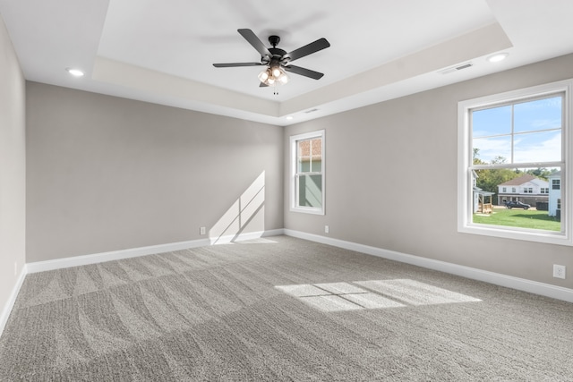 unfurnished room with a wealth of natural light, ceiling fan, carpet flooring, and a raised ceiling