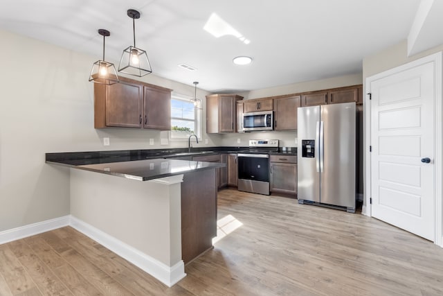 kitchen with light hardwood / wood-style floors, sink, kitchen peninsula, appliances with stainless steel finishes, and pendant lighting